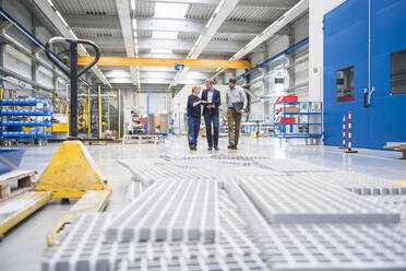 Two men and a woman walking and talking in a factory - DIGF10499