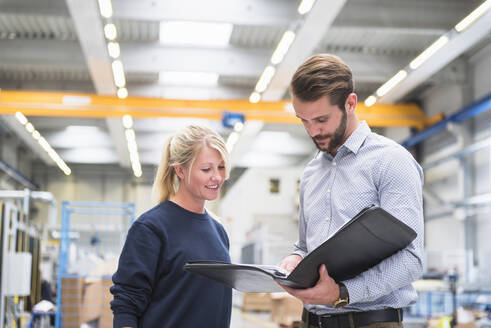 Mann mit Ordner und Frau in einer Fabrik - DIGF10501