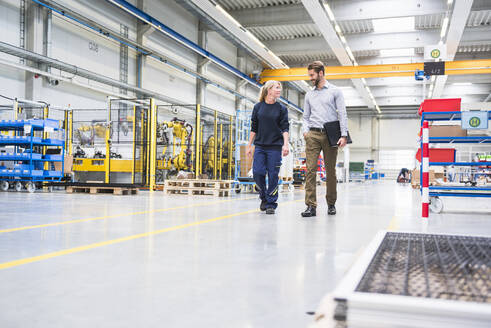 Mann und Frau gehen und sprechen in einer Fabrik - DIGF10505