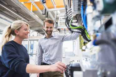 Lächelnder Mann und lächelnde Frau an einer Maschine in einer Fabrik - DIGF10509