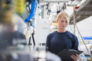 Portrait of young woman holding clipboard in a factory - DIGF10511