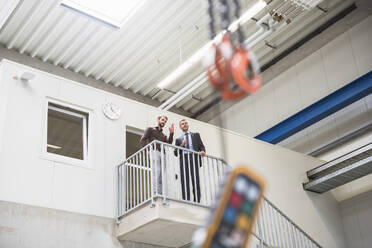 Zwei Geschäftsleute unterhalten sich im Obergeschoss einer Fabrik - DIGF10535