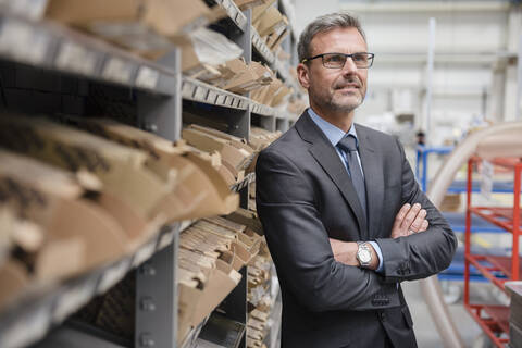 Porträt eines selbstbewussten reifen Geschäftsmannes an einem Regal in einer Fabrik, lizenzfreies Stockfoto