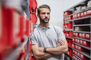 Junger Mann lehnt an einem Regal in einer Fabrik - DIGF10570