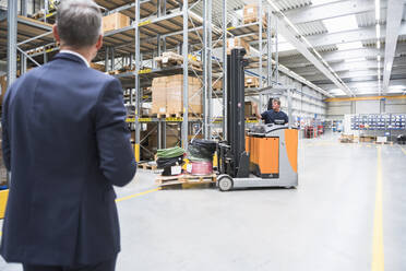 Businessman and worker with forklift in high rack warehouse - DIGF10592