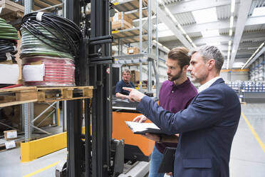 Zwei Männer und ein Arbeiter auf einem Gabelstapler in einem Hochregallager - DIGF10604