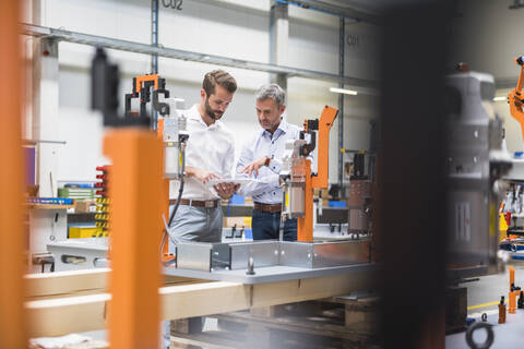 Zwei Männer teilen sich ein Tablet in einer Fabrikhalle, lizenzfreies Stockfoto