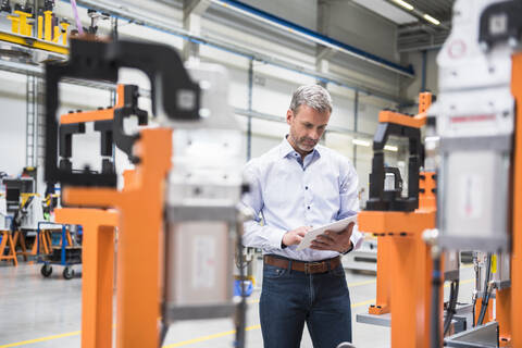 Älterer Mann benutzt Tablet in der Fabrikhalle, lizenzfreies Stockfoto