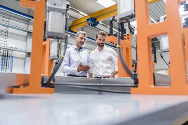 Two men with tablet looking at machine on factory shop floor - DIGF10617