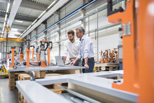 Zwei Männer benutzen einen Laptop in einer Fabrikhalle - DIGF10629