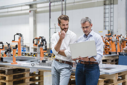 Zwei Männer benutzen einen Laptop in einer Fabrikhalle - DIGF10630