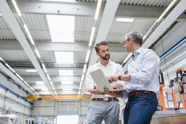 Two men using laptop on factory shop floor - DIGF10632