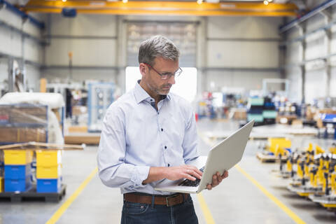 Mature man using laptop on factory shop floor stock photo