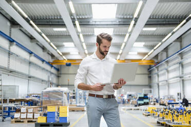 Junger Mann mit Laptop in einer Fabrikhalle - DIGF10636