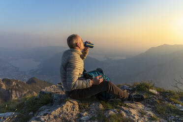 Hiker drinking on viewpoint at sunset, Orobie Alps, Lecco, Italy - MCVF00308