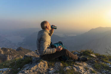 Wanderer trinkt auf einem Aussichtspunkt bei Sonnenuntergang, Orobie Alpen, Lecco, Italien - MCVF00308