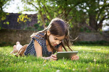Lächelndes Mädchen, das auf einer Wiese im Garten liegt und ein digitales Tablet benutzt - LVF08871