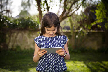 Lächelndes Mädchen, das im Garten steht und ein digitales Tablet benutzt - LVF08872