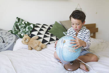 Porträt eines kleinen Jungen auf dem Bett sitzend mit seinem Globus - HMEF00923
