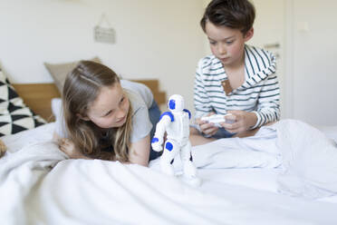 Brother and sister crouching on bed playing with toy robot - HMEF00937