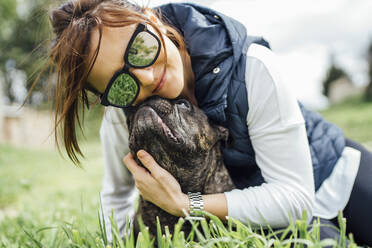 Porträt einer glücklichen Frau, die ihre Bulldogge auf einer Wiese knuddelt - OCMF01213