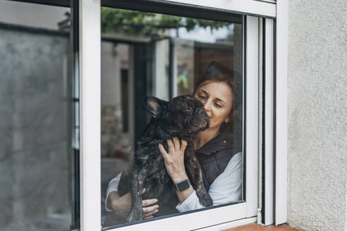 Frau, die ihre Bulldogge hinter dem Fenster streichelt - OCMF01217