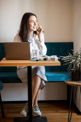 Portrait of smiling young woman on the phone working at home office - DAWF01442