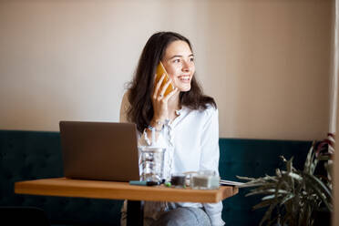 Portrait of smiling young woman on the phone working at home office - DAWF01443