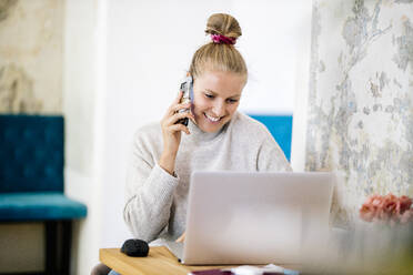 Portrait of smiling blond woman on the phone using laptop - DAWF01482