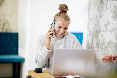 Porträt einer lächelnden blonden Frau am Telefon mit Laptop - DAWF01482