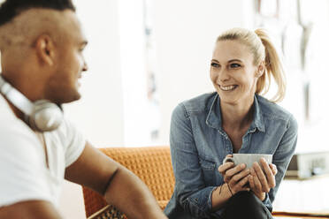 Porträt einer glücklichen blonden Frau mit Kaffeetasse, die einem Freund zuhört - DAWF01507