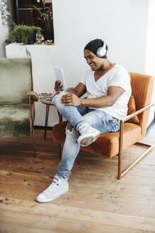 Lachender Mann mit Mini-Tablet und Kopfhörern zu Hause - DAWF01514