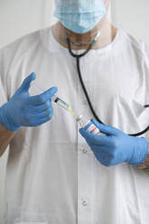 Mann in Schutzkleidung bei der Vorbereitung der Covid-19-Impfung - SNF00140
