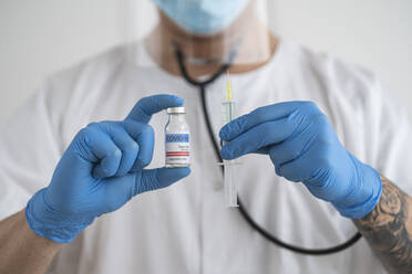 Mann in Schutzkleidung mit Covid-19-Impfstoff und Spritze - SNF00141