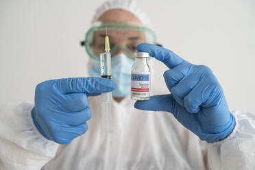 Woman in protective wear holding covid-19 vaccine and syringe - SNF00149