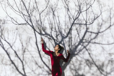 Frau in rotem Kleid mit Tänzerin Pose und Baum Schatten an der Wand - TCEF00620