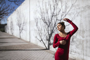 Frau in rotem Kleid mit Tänzerin Pose und Baum Schatten an der Wand - TCEF00621