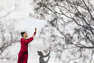 Frau in rotem Kleid mit Tänzerin Pose und Baum Schatten an der Wand - TCEF00622