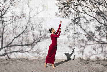 Frau in rotem Kleid mit Tänzerin Pose und Baum Schatten an der Wand - TCEF00623