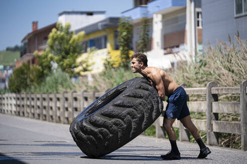 Athlete with an amputated arm exercising with tractor tire on a road - SNF00187