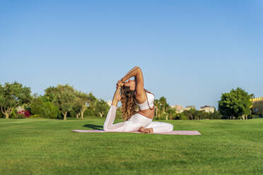 Frau macht Yoga auf einer Matte auf dem Rasen - DLTSF00678