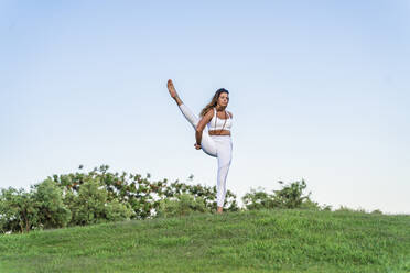 Woman doing yoga on a meadow lifting her leg - DLTSF00680