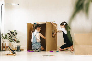 Two little sisters building house with cardboard box - ERRF03672