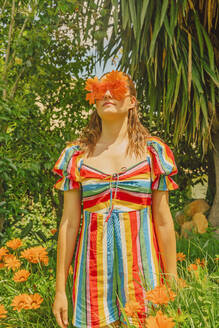 Portrait of woman in nature wearing glasses with orange flowers covering her eyes - ERRF03690