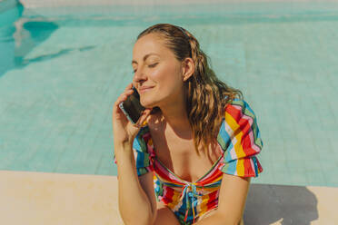 Portrait of happy woman on the phone sitting at poolside - ERRF03702