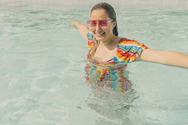 Porträt einer gekleideten Frau mit farbiger Sonnenbrille, die sich im Schwimmbad entspannt - ERRF03721