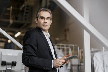 Portrait of mature businessman holding tablet in a factory - DIGF10653