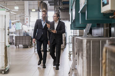 Two businessmen with tablet walking in a factory - DIGF10669