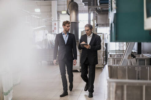 Zwei Geschäftsleute mit Tablet zu Fuß in einer Fabrik - DIGF10670