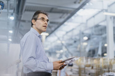 Mature businessman with documents and tablet in a factory - DIGF10703